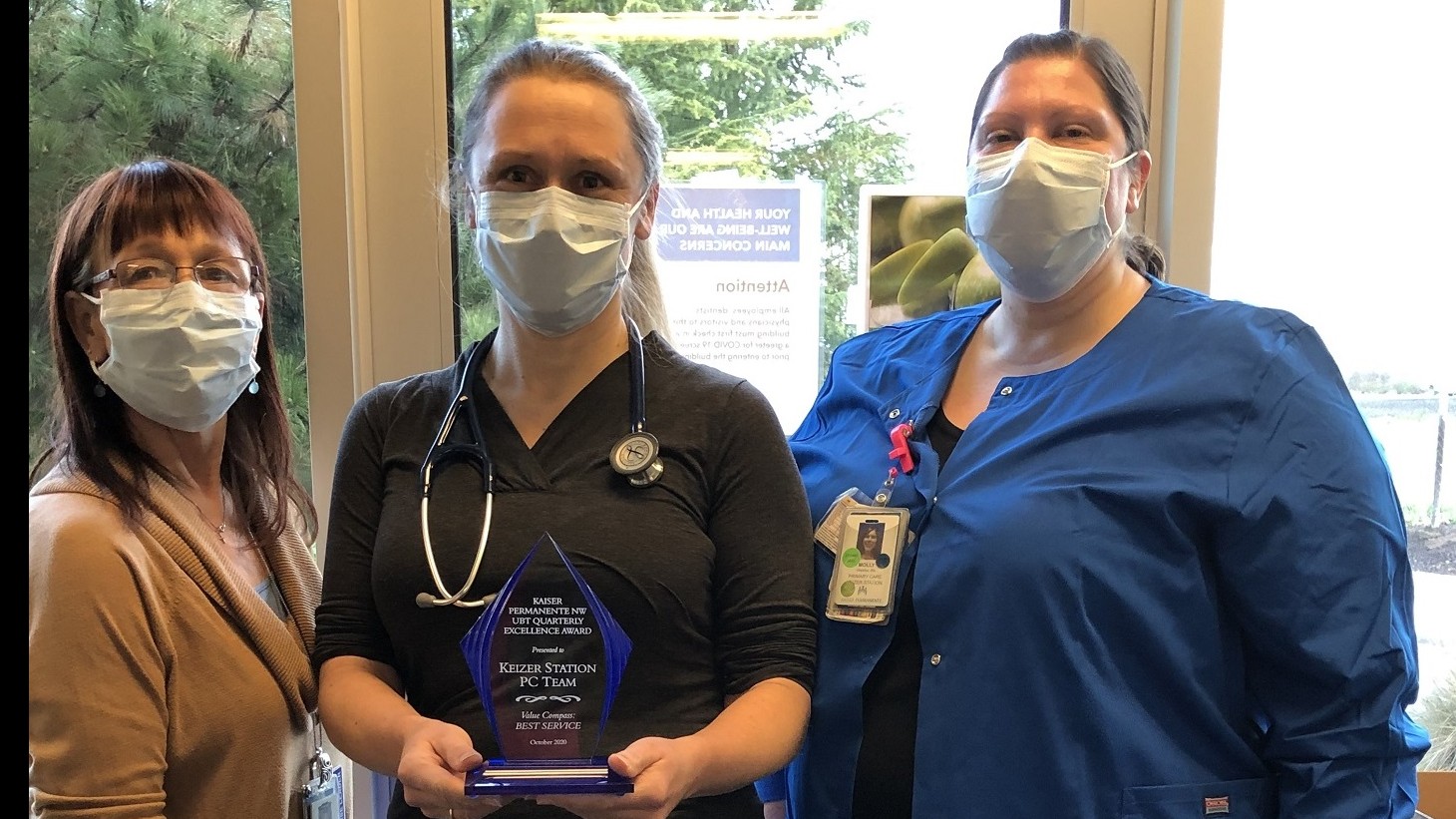 3 women, wearing mask, posing with an award