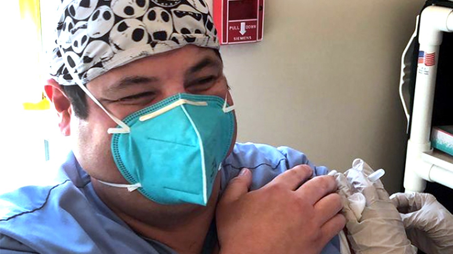 Young Latino man, wearing a blue mask, getting a vaccine 