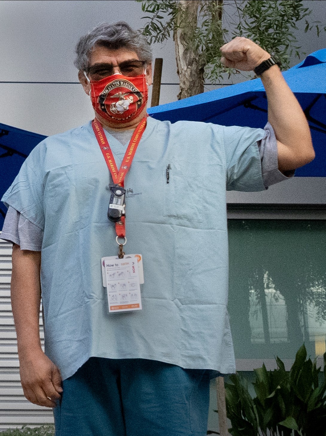 Man in scrubs, wearing a face mask, with left arm raised in a fist