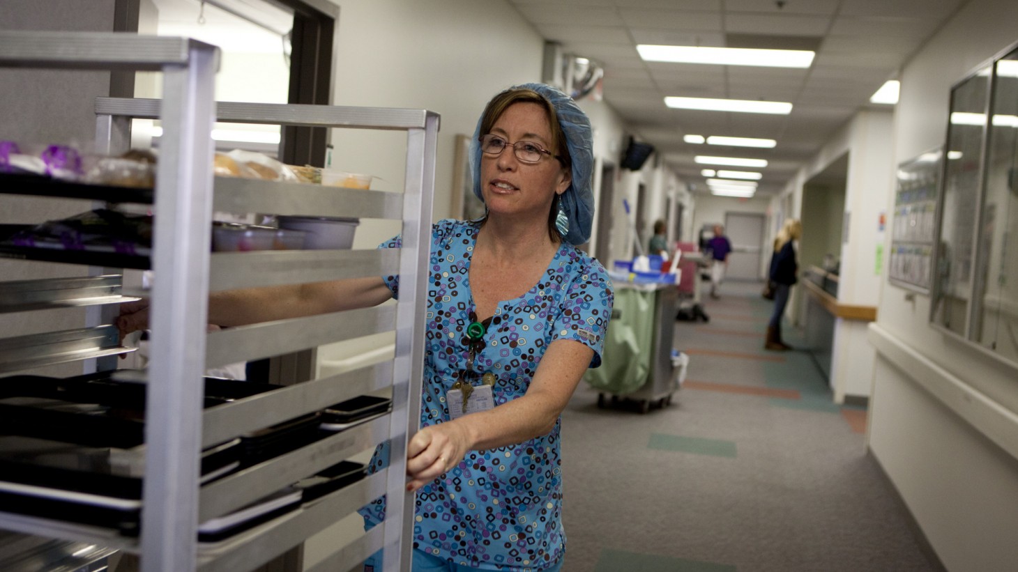 Nutrition aide pushing a cart of meals. 