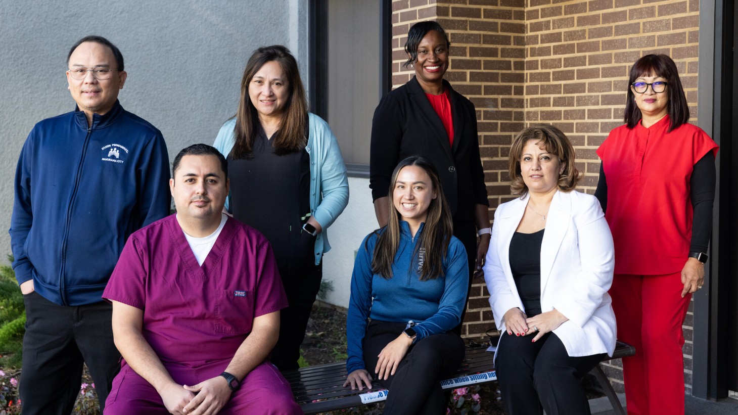 Group portrait of seven health care workers, posing in front of a brick building